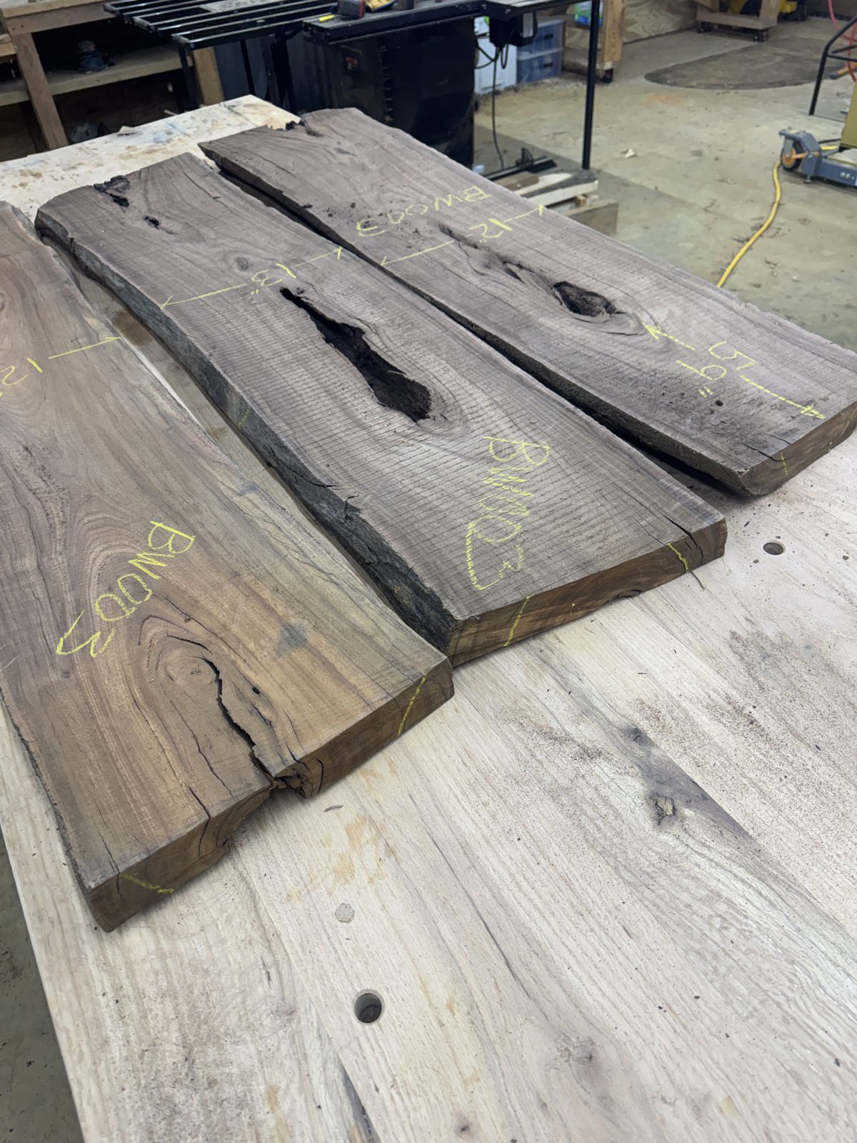 Three BW003 walnut slabs laid out on the shop table, with yellow crayon width and length marks