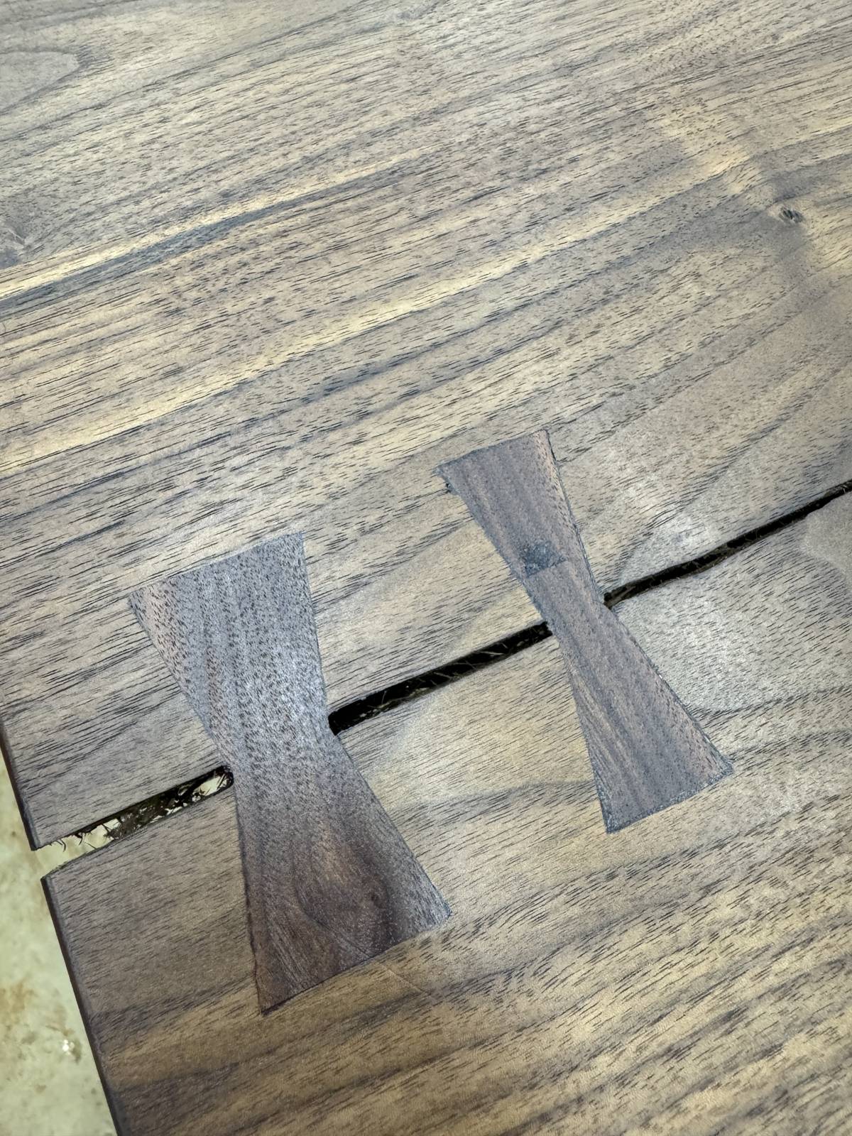 Close-up of two dark walnut bowtie inlays across a crack in a tabletop