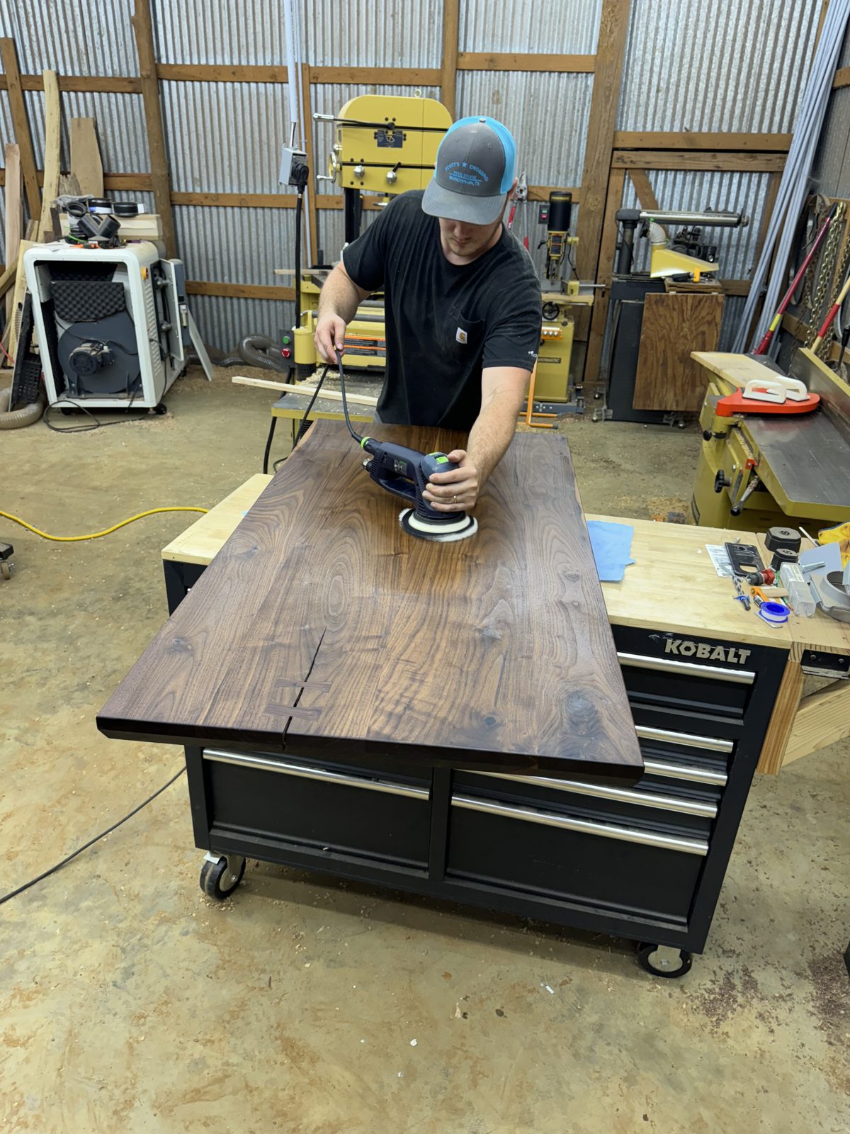 Sanding a dark walnut tabletop with a random-orbit sander on a rolling tool cabinet