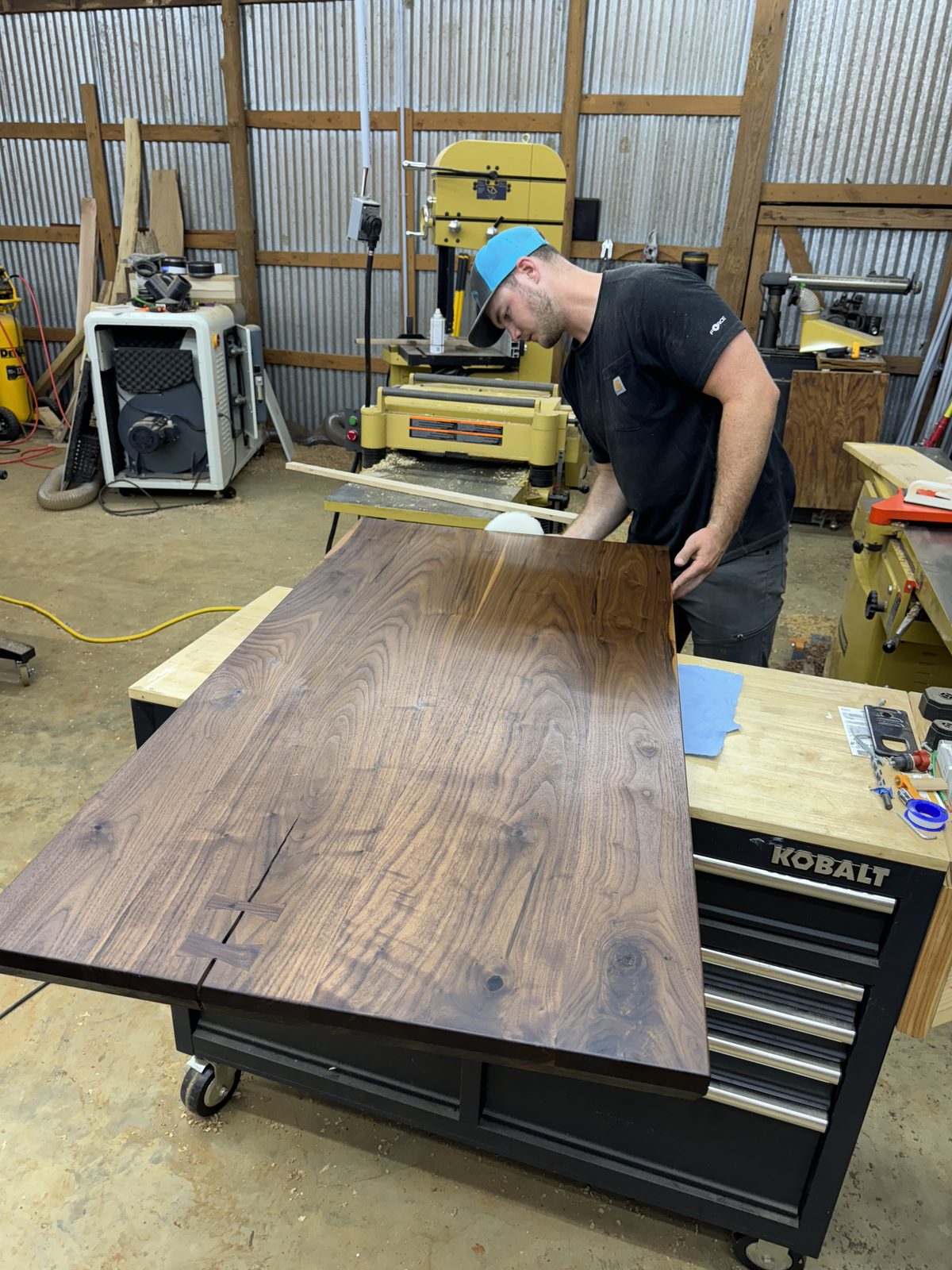 Walnut tabletop with bowtie inlays being worked on a rolling tool cabinet in the shop